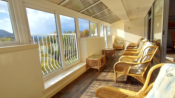 A sunlit room with large windows, wicker furniture, and a view of a mountainous landscape. - Loch Rannoch Highland Club, Highland Lodge 8 (Kinloch Rannoch)