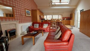 A spacious living room with a fireplace, red leather sofas, and a dining area with wooden furniture. - Loch Rannoch Highland Club, Highland Lodge 46 (Kinloch Rannoch)