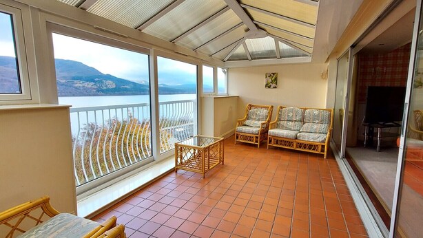 A balcony with wicker furniture, a glass table, and a view of mountains. - Loch Rannoch Highland Club, Highland Lodge 46 (Kinloch Rannoch)