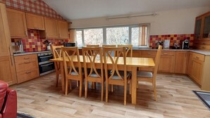 A kitchen with wooden cabinets, a dining table with chairs, and a red leather chair. - Loch Rannoch Highland Club, Highland Lodge 46 (Kinloch Rannoch)
