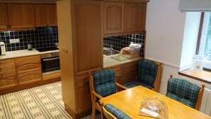 Een compacte keuken met houten kastjes, een inbouwoven en een eethoek met geruite stoelen.