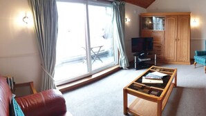 Een woonkamer met een grote schuifpui, een televisie, een houten kast en een rode leren bank.