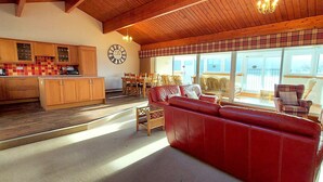 Ein geräumiger Wohnbereich mit einem roten Ledersofa, Holzmöbeln und einer Küche im Hintergrund.