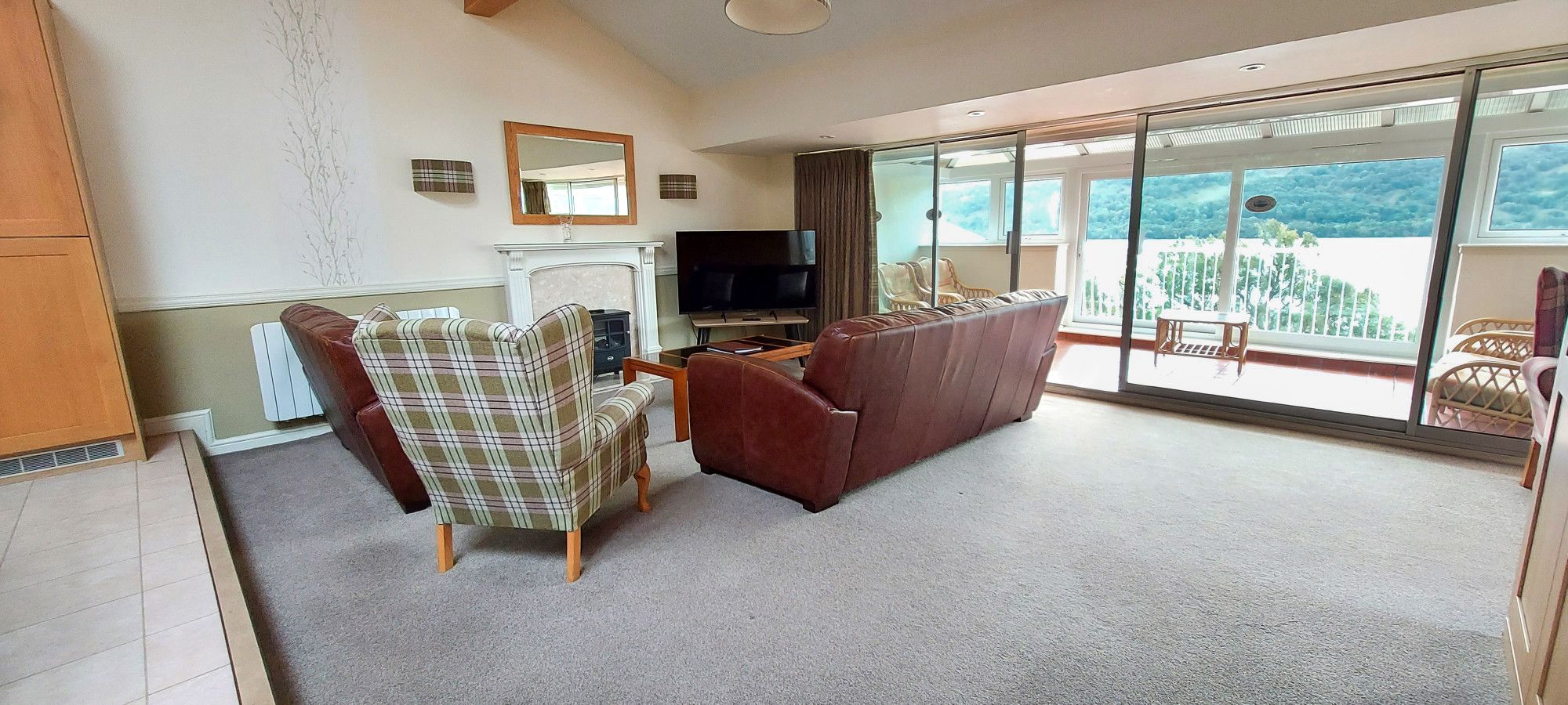 A living room with a fireplace, a television, and a large sliding glass door leading to a balcony.