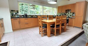 A kitchen with wooden cabinets, a dining table with chairs, and a window with a view of greenery.