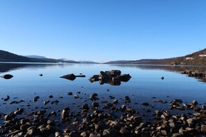 A calm lake with scattered rocks and mountains in the background. - Loch Rannoch Highland Club, Highland Lodge 44 (Kinloch Rannoch)