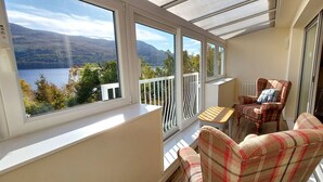 A balcony with a view of a lake and mountains, furnished with a chair and a small table. - Loch Rannoch Highland Club, Pine Martin Lodge 4 (Kinloch Rannoch)