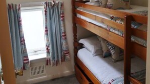 Un dormitorio pequeño y funcional con una cama litera, una ventana con cortinas y un radiador.