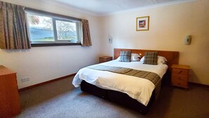 A bedroom with a bed, bedside tables, a nightstand, a window with curtains, and a framed picture on the wall. - Loch Rannoch Highland Club, Red Squirrel 4 (Kinloch Rannoch)
