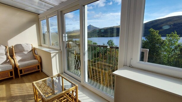 A balcony with wicker furniture, a glass table, and a view of a lake and mountains. - Loch Rannoch Highland Club, Red Squirrel 4 (Kinloch Rannoch)