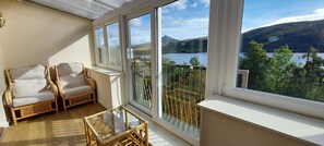 A balcony with wicker furniture, a glass table, and a view of a lake and mountains. - Loch Rannoch Highland Club, Red Squirrel 4 (Kinloch Rannoch)