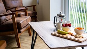 A cozy room with a wooden table, chairs, a coffee maker, and a view of greenery through a window. - Loch Rannoch Highland Club, Red Squirrel Lodge 8 (Kinloch Rannoch)