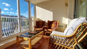 A balcony with a view of mountains, a wicker chair, a sofa, and a glass-top table. - Loch Rannoch Highland Club, Studio 5 (Kinloch Rannoch)