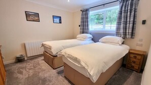Een slaapkamer met twee bedden, een raam met gordijnen, een radiator en een klein houten nachtkastje.