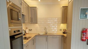 A modern kitchen with white cabinets, stainless steel appliances, and a wooden floor. - Loch Rannoch Highland Club, Pine Martin Lodge 2 (Kinloch Rannoch)