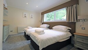 A hotel room with two beds, a window with curtains, a radiator, and a dresser. - Loch Rannoch Highland Club, Pine Martin Lodge 2 (Kinloch Rannoch)