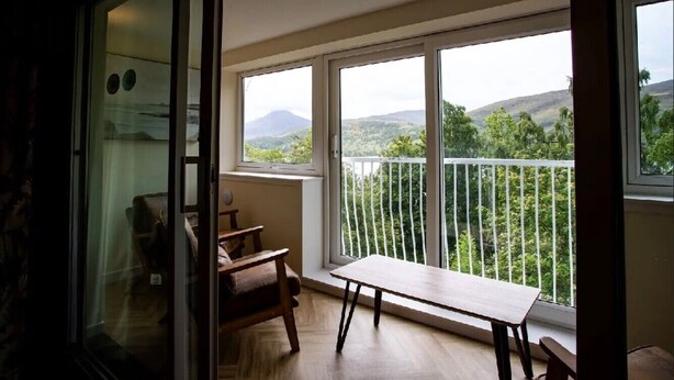 A balcony with a wooden table and chairs, a glass door, and a view of green hills. - Loch Rannoch Highland Club, Red Squirrel lodge 3 (Kinloch Rannoch)