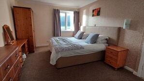 A bedroom with a bed, a dresser, a nightstand, a window with curtains, and a painting on the wall. - Loch Rannoch Highland Club. Highland Lodge 5 (Kinloch Rannoch)