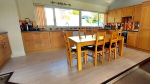 A kitchen with wooden cabinets, a dining table with chairs, and a window providing a view of the outside. - Loch Rannoch Highland Club. Highland Lodge 5 (Kinloch Rannoch)