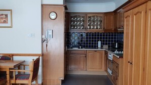 Een kleine keuken met houten kastjes, een inbouwmagnetron en een betegelde spatwand.