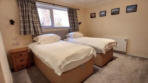 Habitación doble con dos camas, una mesita de noche pequeña, un radiador y una ventana con cortinas.