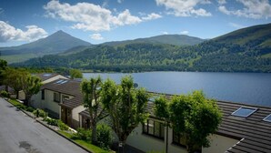 A lakeside view with a mountain in the background, a row of houses with sloped roofs, and a clear sky. - Rannoch Highland Club, Pine Martin Lodge 6 (Kinloch Rannoch)
