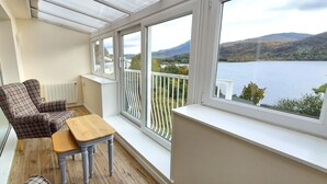 A balcony with a view of a lake and hills, furnished with a chair and a small table. - Rannoch Highland Club, Pine Martin Lodge 6 (Kinloch Rannoch)