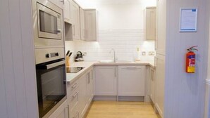 A compact kitchen with white cabinets, a built-in oven, and a microwave. - Rannoch Highland Club, Pine Martin Lodge 6 (Kinloch Rannoch)