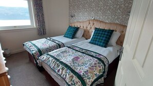 A hotel room with two beds, floral bedspreads, a wooden dresser, and a window with a view. - Loch Rannoch Highland Lodge 7 (Kinloch Rannoch)