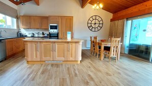 A kitchen with wooden cabinets, a central island, and a dining area with chairs. - Loch Rannoch Highland Lodge 7 (Kinloch Rannoch)