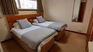 A double room with two beds, a window with curtains, a mirror, and a wooden wardrobe.
