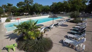A pool area with lounge chairs and a palm tree. - Mobile home with air conditioning near the ocean and plenty of places to explore (La Tremblade)