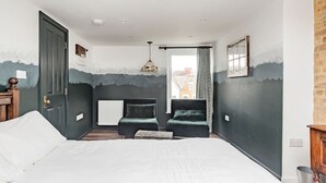 Un dormitorio con cama, dos sillas, un radiador y una ventana con cortinas.