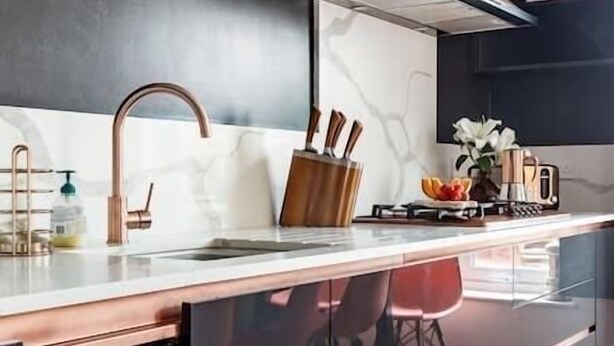 Una cocina moderna con grifo de cobre, una lámpara de pared y una campana extractora de acero inoxidable.