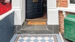 Una puerta negra con paneles de vidrio decorativos y un tirador de latón, flanqueada por columnas blancas con un emblema circular.