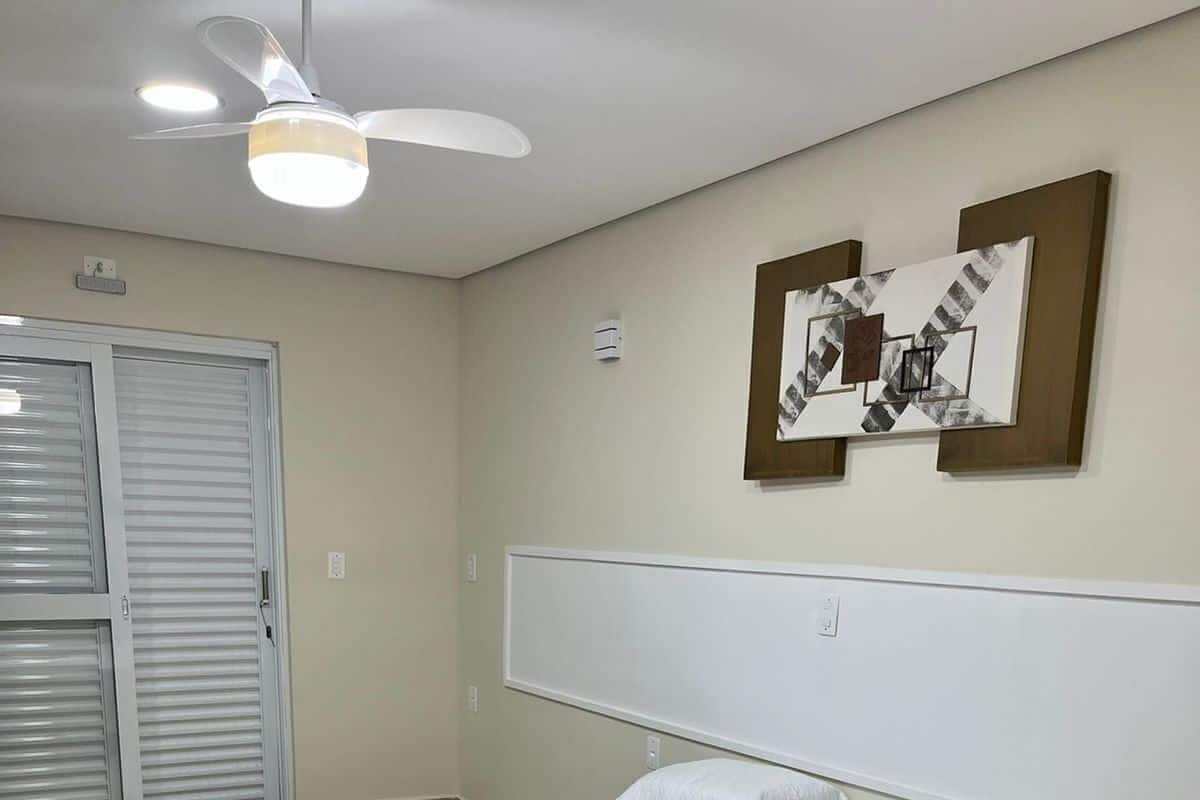 A bedroom with a bed, a ceiling fan, a door, and a wall-mounted picture.