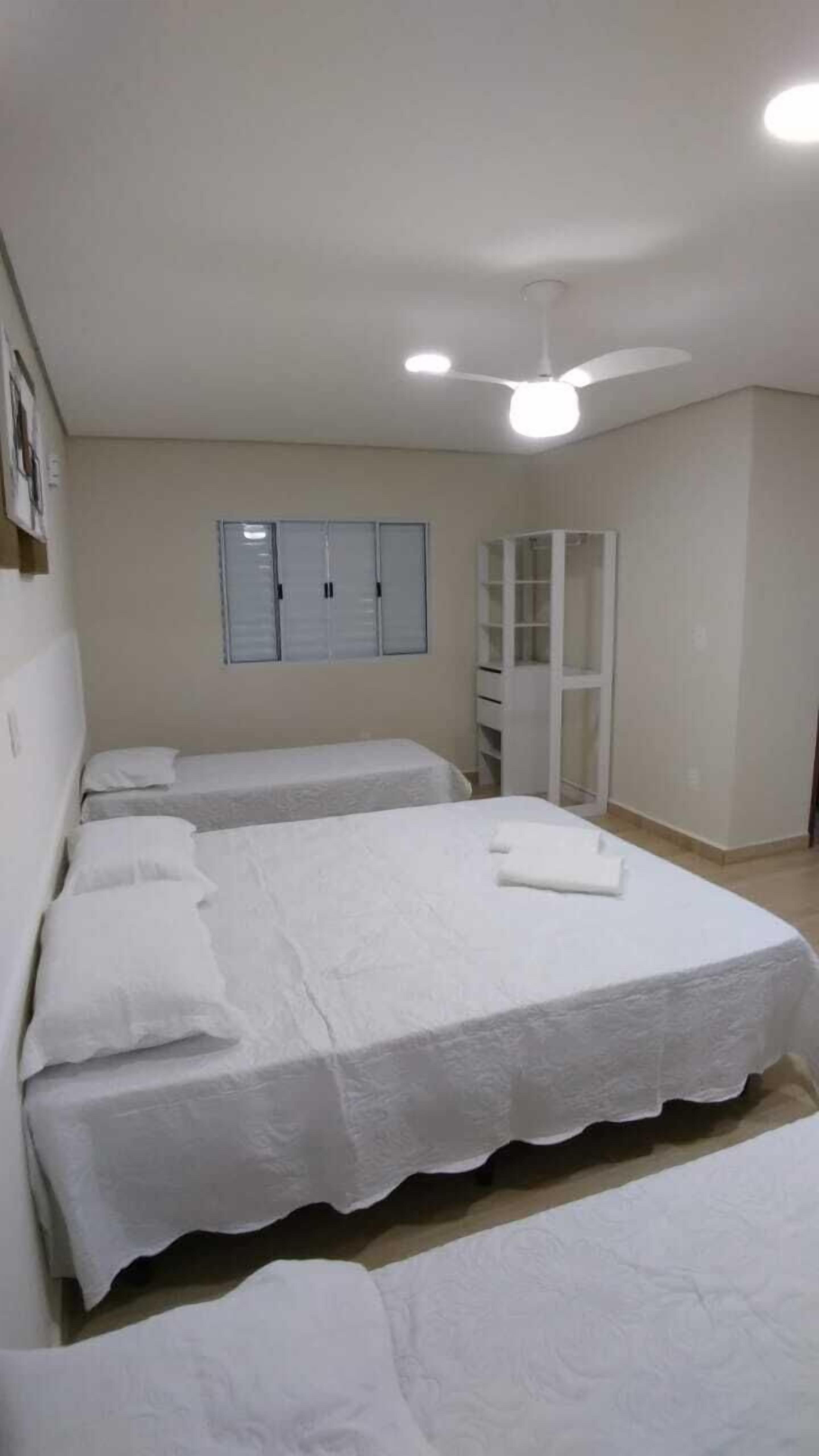 A bedroom with two beds, a ceiling fan, a wardrobe, and a window with blinds.