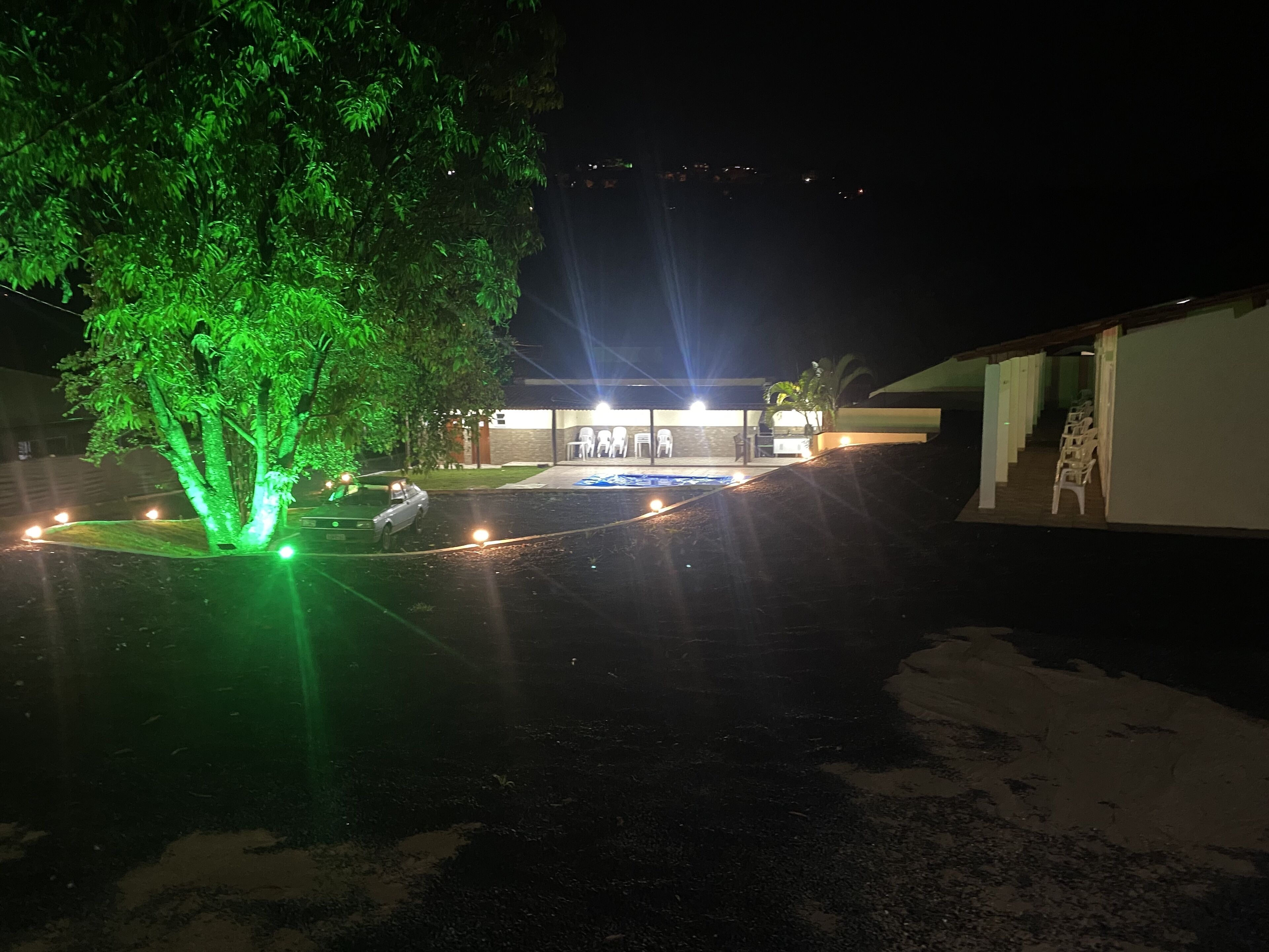 Vista nocturna de un edificio con piscina, rodeado de árboles con iluminación verde.