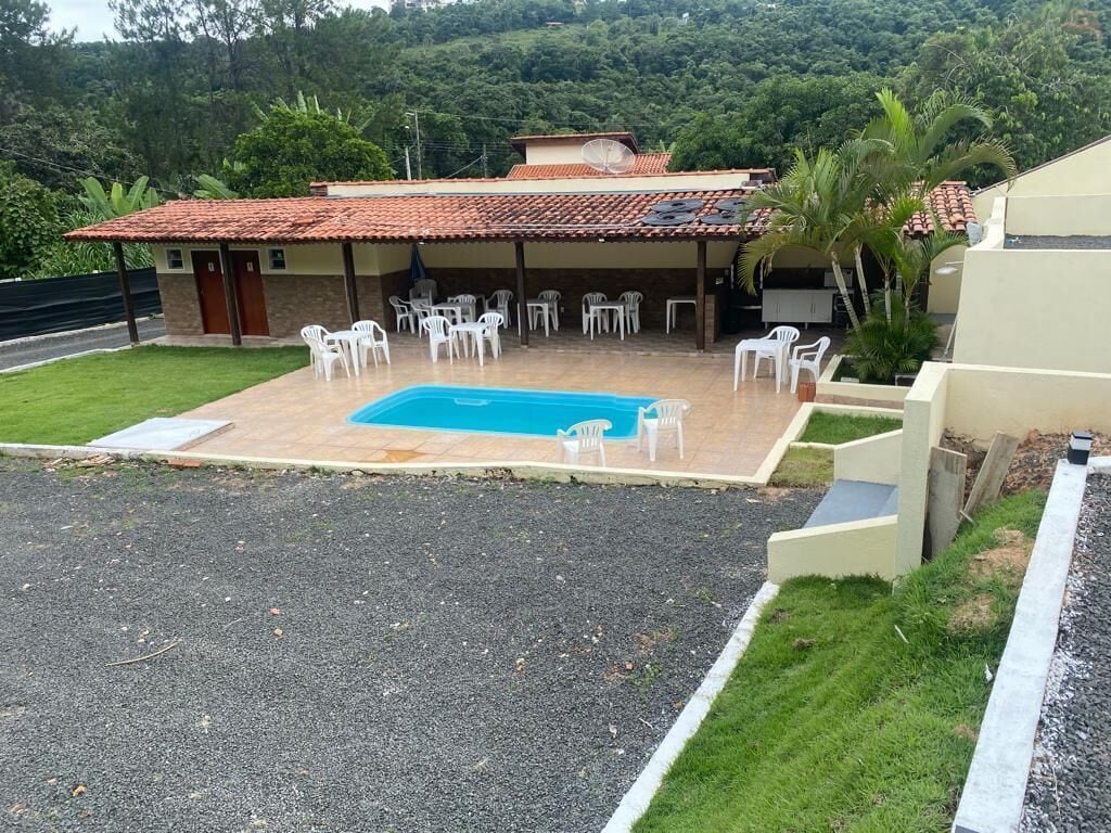 A pool area with a tiled roof, white plastic chairs, and a small building with a door.