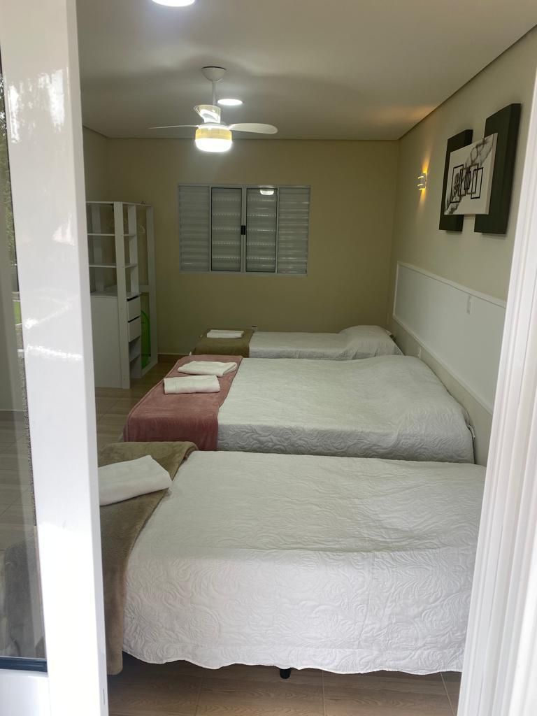 A room with three beds, a ceiling fan, and a wall-mounted light fixture.