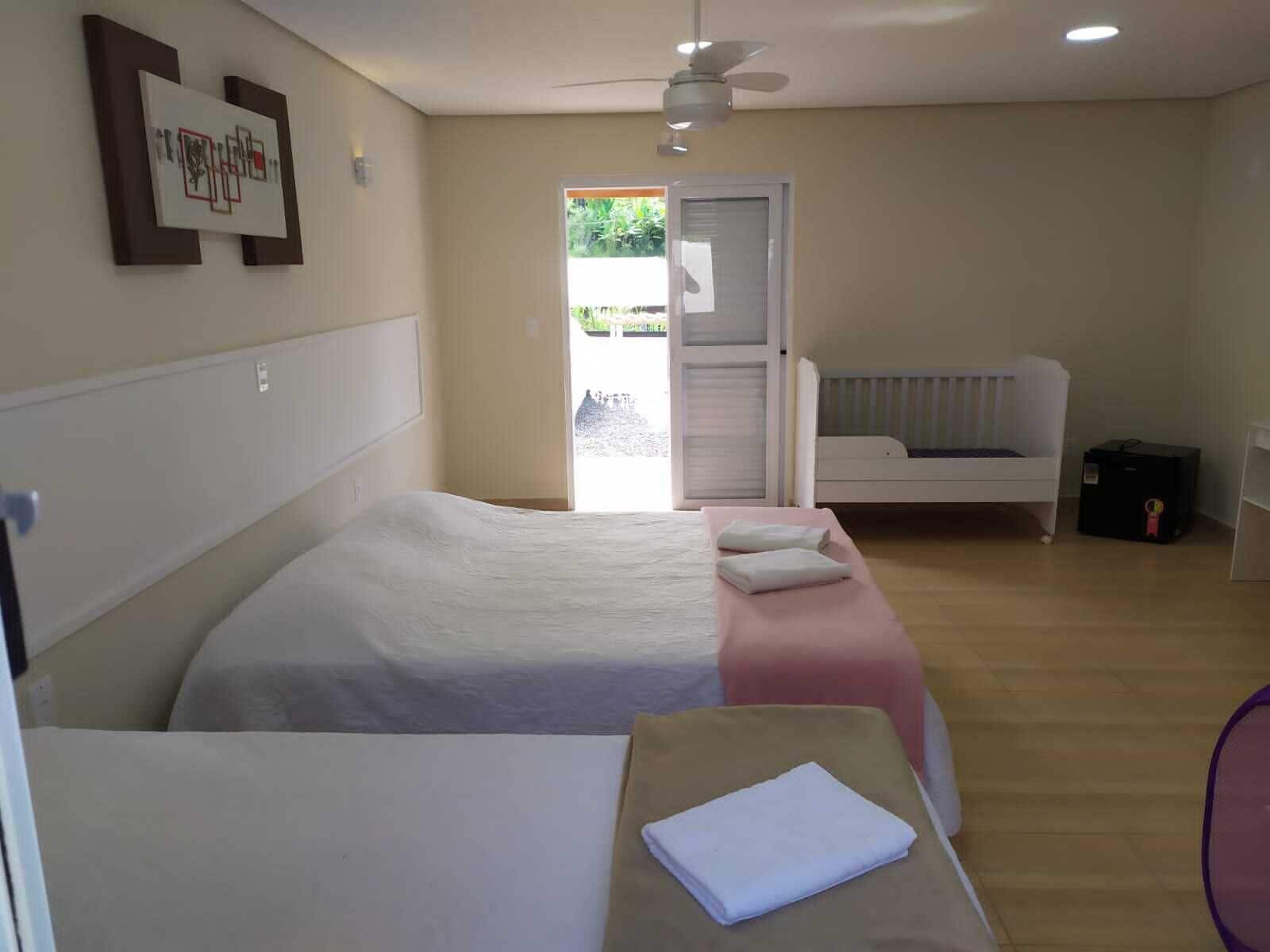Habitación de hotel con dos camas, ventilador de techo, ventana con vistas a zonas verdes y puerta que da al exterior.