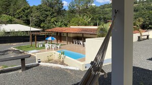 Zona de piscina con techo de baldosas, mobiliario exterior y vistas a la vegetación y colinas circundantes.