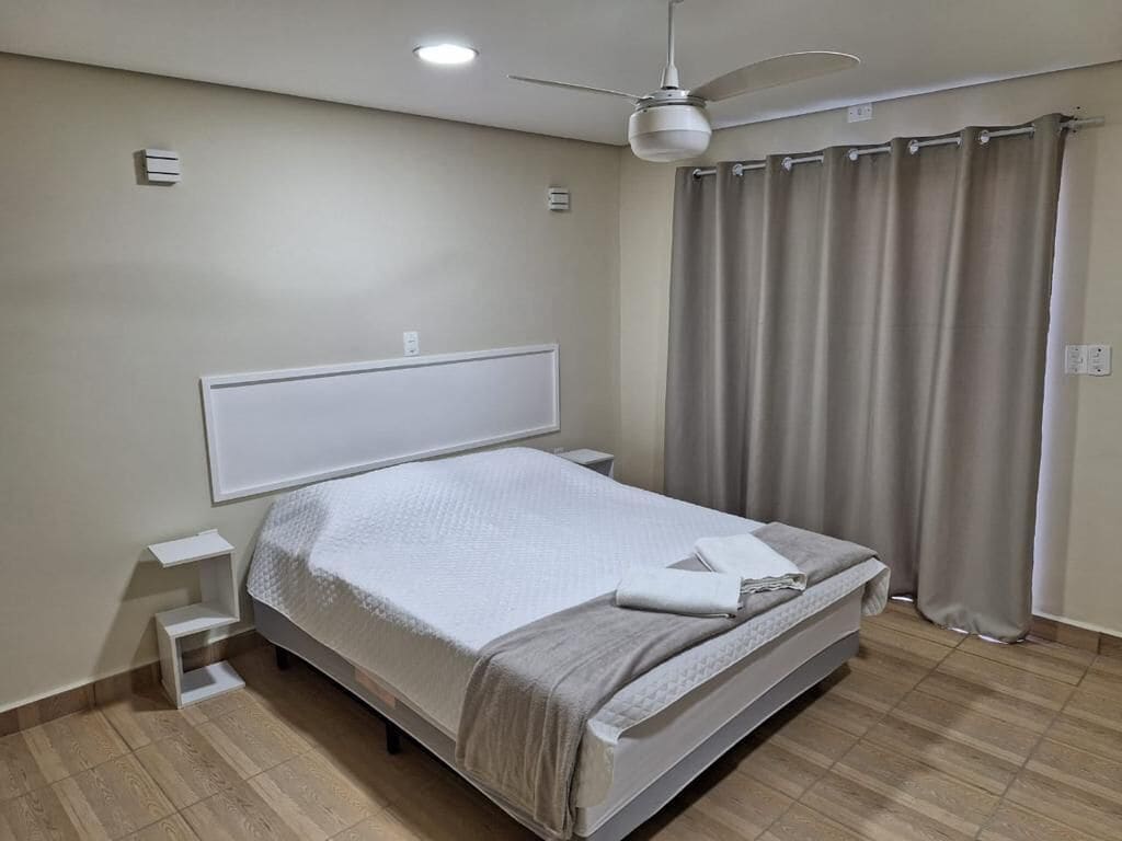 A bedroom with a bed, a bedside table, a ceiling fan, and a window with curtains.