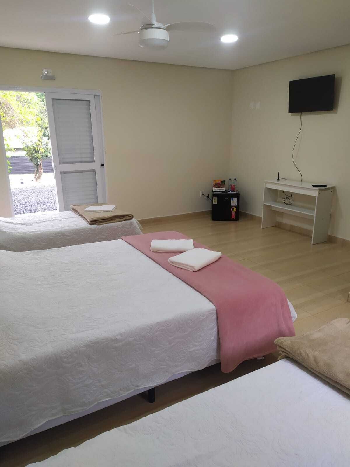 A hotel room with two beds, a desk, a television, and a door leading outside.