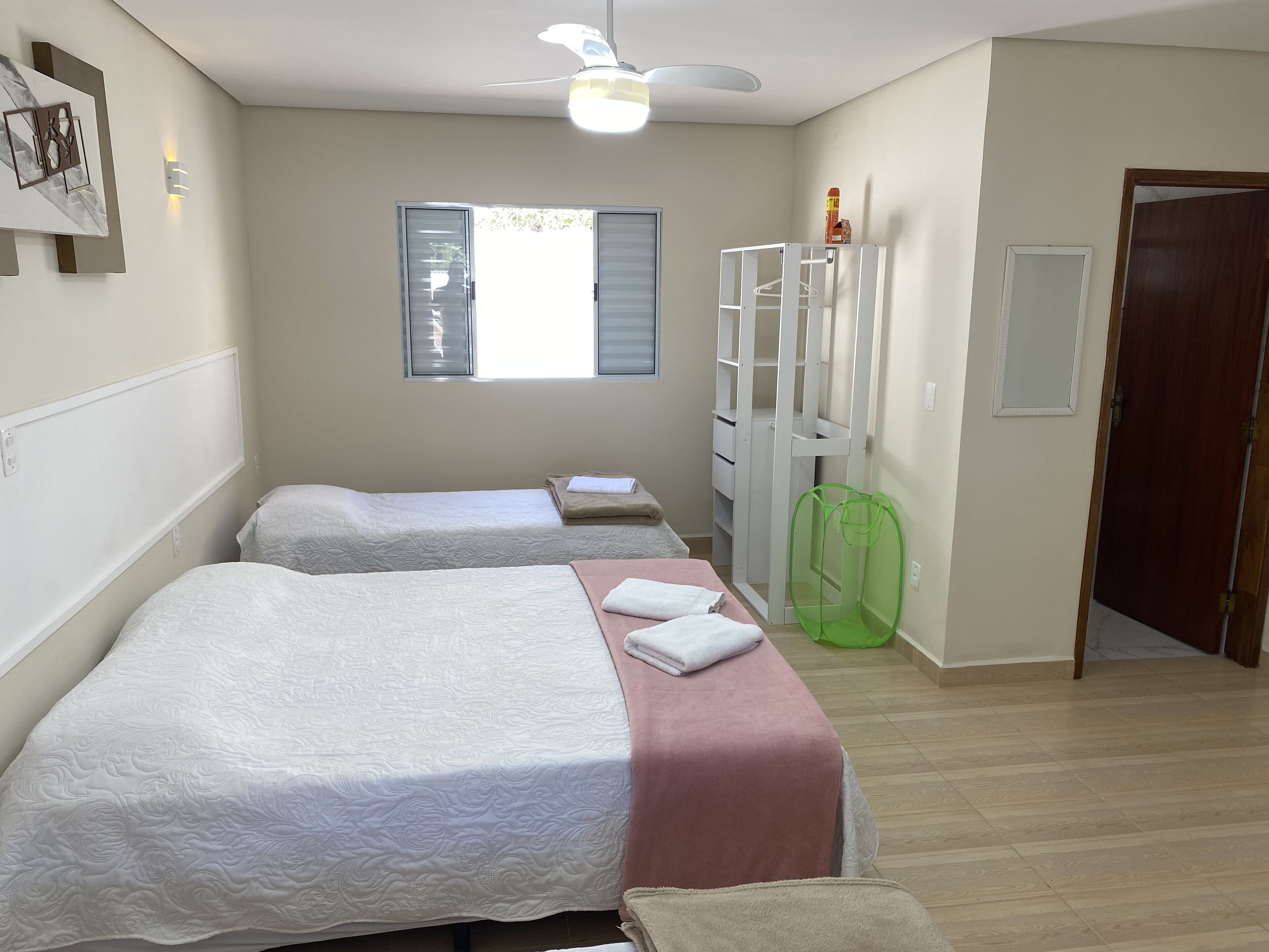 A hotel room with two beds, a ceiling fan, a window with blinds, a wardrobe, and a door.
