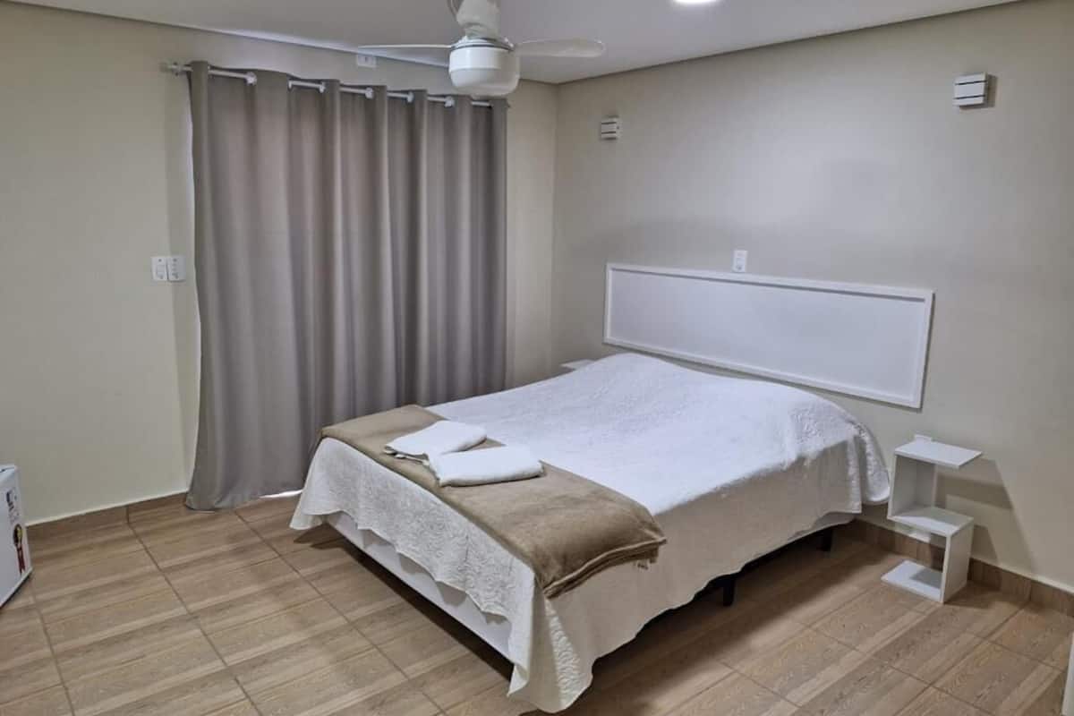 A bedroom with a bed, a ceiling fan, a window with curtains, and a bedside table.