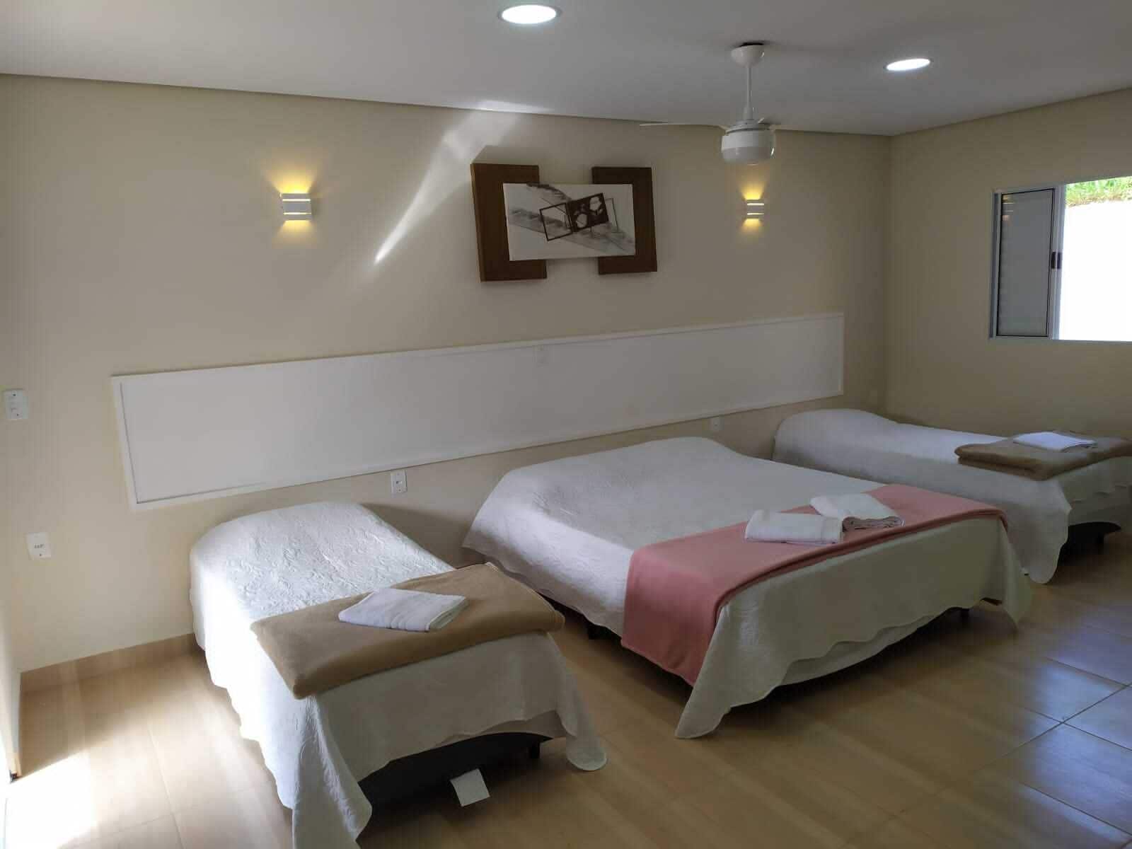 Habitación de hotel con dos camas, ventilador de techo, luces fijadas en la pared y una ventana.