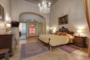 A spacious bedroom with a large bed, ornate chandelier, and classic decor.