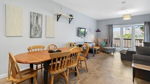 Un comedor con una mesa y sillas de madera, un televisor montado en la pared y un sofá en la sala de estar.