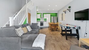 Una sala de estar moderna con un sofá gris, una mesa de comedor de madera y una escalera que sube a otro nivel.